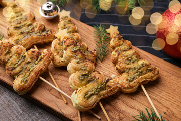 Christmas trees made with puff pastry, pesto sauce, cheese and festive decor on wooden table, closeup