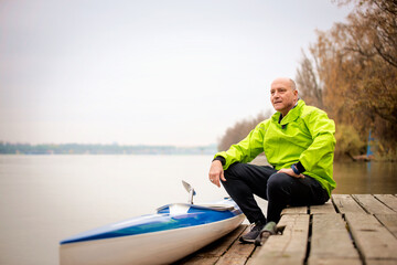 Fototapeta premium Sporty active senior sitting on the jetty by the river next to his kayak
