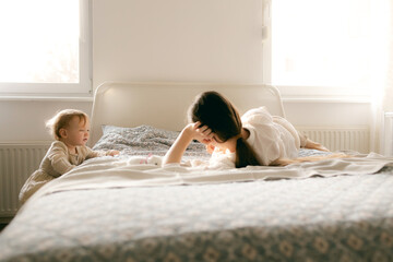 Young happy mother playing with cute little child girl in the living room at home. Woman parent spending time with daughter. Family leisure and people concept