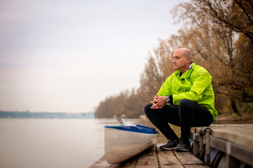 Fototapeta premium Sporty active senior sitting on the jetty by the river next to his kayak