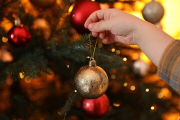 Little boy decorating Christmas tree at home, closeup. Bokeh effect