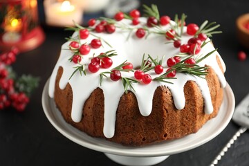 Tasty Christmas cake with icing, cranberries and rosemary on black table, closeup