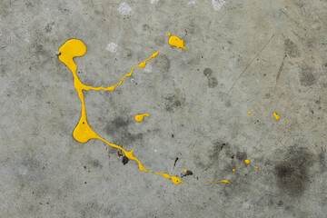 A dynamic splatter of bright yellow paint contrasts sharply against a cracked and textured grey concrete surface