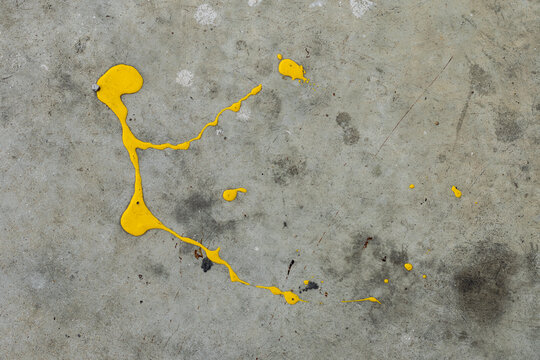 A dynamic splatter of bright yellow paint contrasts sharply against a cracked and textured grey concrete surface