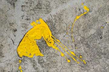 A dynamic splatter of bright yellow paint contrasts sharply against a cracked and textured grey concrete surface