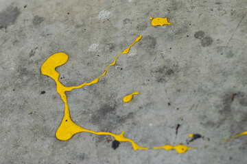 A dynamic splatter of bright yellow paint contrasts sharply against a cracked and textured grey concrete surface
