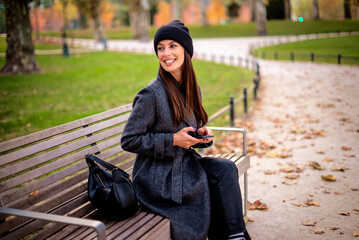 Confident middle-aged woman sitting in a park in an autumn day and using smartphone