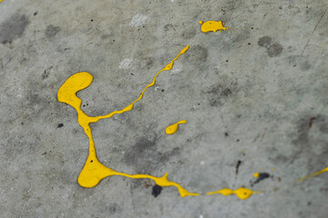 A dynamic splatter of bright yellow paint contrasts sharply against a cracked and textured grey concrete surface