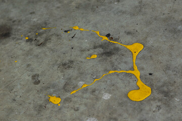 A dynamic splatter of bright yellow paint contrasts sharply against a cracked and textured grey concrete surface