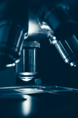 Macro photo of optical microscope lens focusing on sample slide under sterile laboratory lighting. Symbolizes technology, research, and medical discovery.