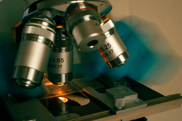 Macro photo of optical microscope lens focusing on sample slide under sterile laboratory lighting. Symbolizes technology, research, and medical discovery.