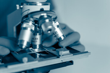 Macro photo of optical microscope lens focusing on sample slide under sterile laboratory lighting. Symbolizes technology, research, and medical discovery.