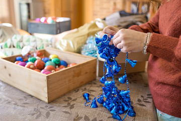 Unrecognizable woman prepares the Christmas decoration and untangles a chain of bright blue bells