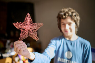 teenage boy holds the main ornament for the Christmas tree, a large, shiny star that will crown the top of the tree. Decorating the house for the Christmas holidays.