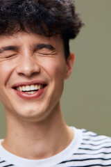 Fototapeta premium smiling man with closed eyes expressing joy and happiness, wearing a striped shirt, youthful style, natural light, green background, casual indoor portrait