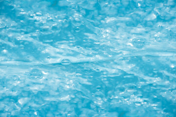 Blue water with ripples on the surface. Defocus blurred transparent blue colored clear calm water surface texture with splashes and bubbles. Water waves with shining pattern texture background.