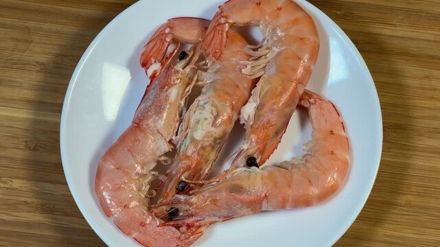 Whole boiled unshelled king prawns on dish on wooden surface
