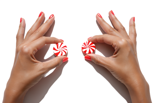 Two female hands with red nail polish holding classic red and white striped peppermint candies against transparent background