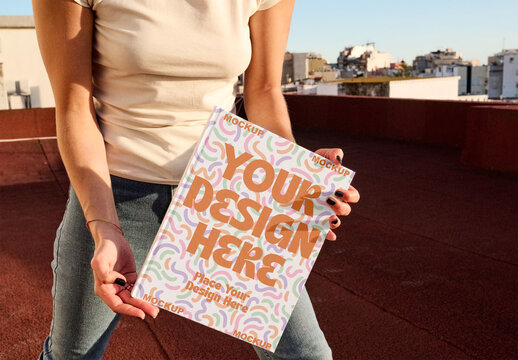 Mockup of Blank Book front cover holding on a Rooftop With a City View During Sunset