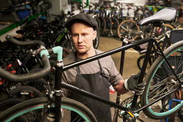 Man wearing gloves repairing bicycle in workshop surrounded by multiple bikes, focusing on adjusting handlebars while standing in bike repair shop