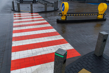 A red and white striped crosswalk stands out on a wet city street, surrounded by modern barriers...