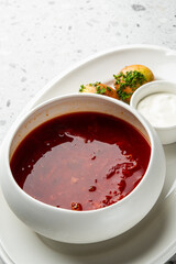 A vibrant bowl of traditional Ukrainian borscht soup with sour cream and garlic buns on a white platter and gray marble table.