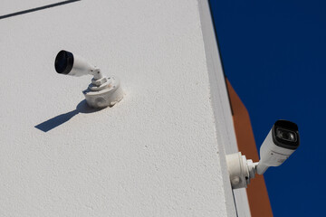 Two security cameras positioned on the side of a building monitor the surrounding area for safety and protection during daytime