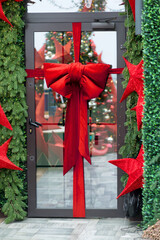 Beautiful red bow tied on a window or exterior door, a Christmas decoration. Warm cozy light inside the house, bokeh lights	