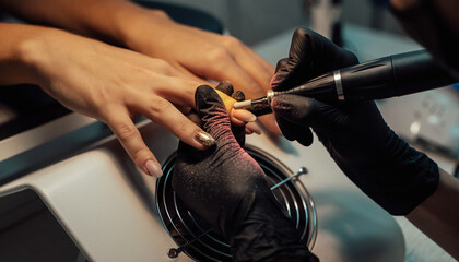 Manicurist removes nail polish uses the electric machine of the nail file during a manicure
