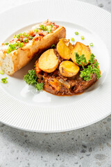 A beautifully plated restaurant-quality meal featuring slow-cooked beef stew topped with roasted potato halves and fresh parsley, served with a side of toasted baguette with toppings.