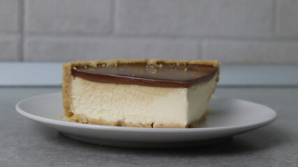 Slice of delicious classic cheesecake on a white plate. Dessert served in a cafe with a blurred background. (128 символів)