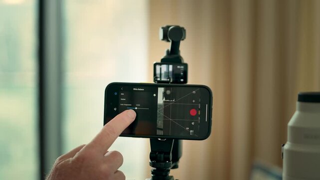 Close-up of a hand adjusting camera settings on a smartphone app. Soft lighting, focused angle, and tech-savvy ambiance enhance the interactive experience.