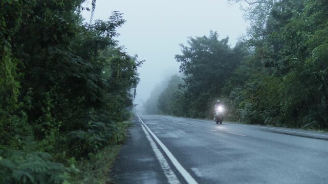 4K footage of a misty mountain road at dawn, featuring thick fog and an oncoming vehicle with glowing headlights creating a cinematic, atmospheric scene.