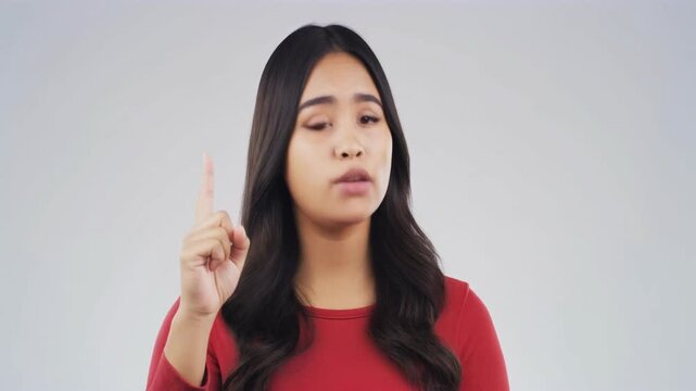 A young woman with long dark hair, wearing a red shirt, points upwards with one finger, looking directly at the viewer.