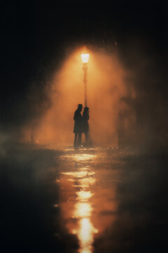 AI-generated image - Silhouette of a couple standing close together under a streetlight during heavy rain, dramatic and moody atmosphere with wet reflections on the ground.