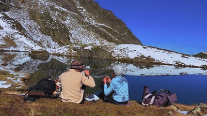 Travelers with Dog by Lake.
Hiking couple with corgi resting and sharing food beside snowy mountain lake.