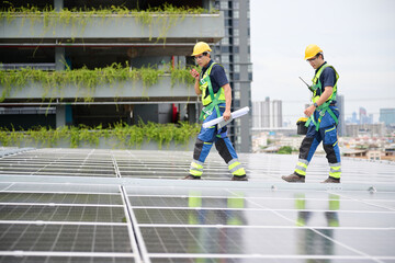 Two construction workers inspecting the solar panels installed on a rooftop, with a clear blue sky background. They are wearing safety gear