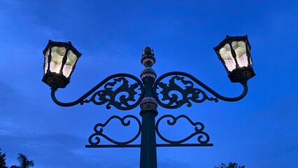 A classic vintage-style street lamp glows under the blue sunset sky. Artistic design with iron...