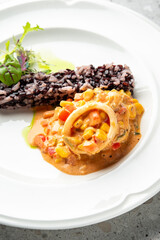 Gourmet black rice dish with creamy vegetable stew & microgreens on white plate