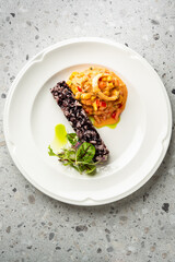 Gourmet black rice dish with creamy vegetable stew & microgreens on white plate