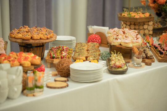 Beautifully arranged buffet table with assorted appetizers, canapes, decorative flowers in warm orange tones. Good for illustrating catering services, celebrations, event organization or festive dinin