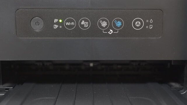 The plastic printer's power button has been pressed and the power light is blue. The internal mechanism is preparing for use, creating a series of mechanical whirring, grinding, and rattling sounds.