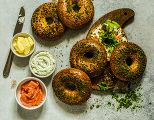 overhead flat lay of everything bagels with sides of butter, cream cheese, and smoked salmon (lox), and a bagel with toppings. breakfast background.