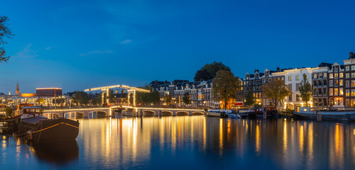 Panorama of Amsterdam at blue hour, historical houses and Magere Brug (Skinny Bridge) reflected in river Amstel
