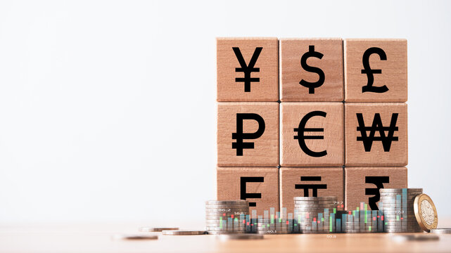 Wooden blocks with global currency symbols stacked beside coins and bar charts representing international finance forex trading investment and global economic exchange concept.