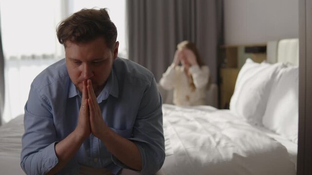 Worried man sitting on bed feeling stressed and insecure, with woman in background looking disappointed, symbolizing male health problems, emotional tension, and relationship difficulties
