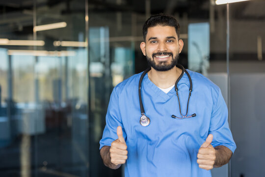 Smiling male doctor wearing scrubs and a stethoscope expressing approval and trust, highlighting excellent medical service and positive healthcare outcomes - Powered by Adobe