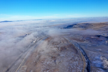 Aerial view of misty countryside hills at wintertime, morning fog above