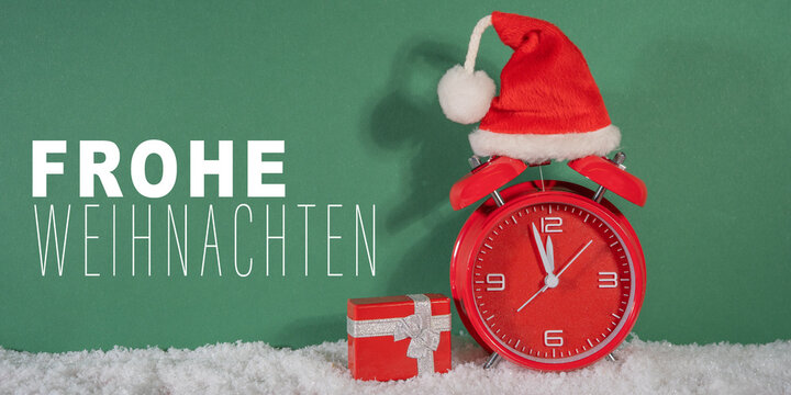 Frohe Weihnachten, Ferien Feier Grußkarte, Karte mit deutschem Text - Countdown Wecker mit Nikolausmütze, Weihnachtsmannmütze und Geschenk im Schnee, grüner Hintergrund - Powered by Adobe