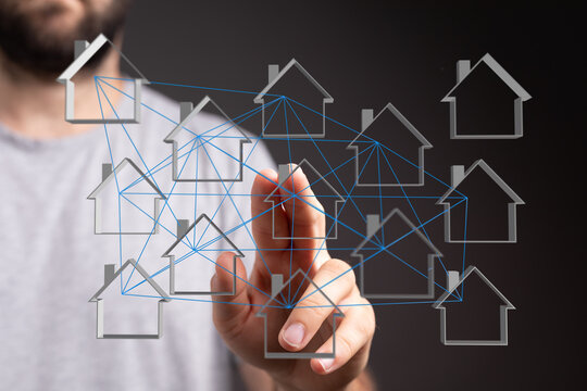 A person's hand interacts with a digital network of house icons.  Concept of interconnected homes, real estate tech, and smart home solutions.